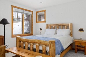 Una cama de madera con cabecera, dos mesitas de noche y una ventana con vistas a un paisaje nevado.