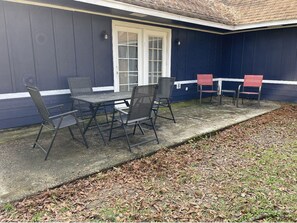 An outdoor seating area with a table and chairs, a door, and a dark blue wall. - Adorable 3 bedroom attached cottage in quiet spot. (Picayune)