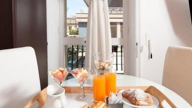 A breakfast tray with pastries, fruits, and juice on a table by a window with a view of buildings. - Fourseasons (Lecce)
