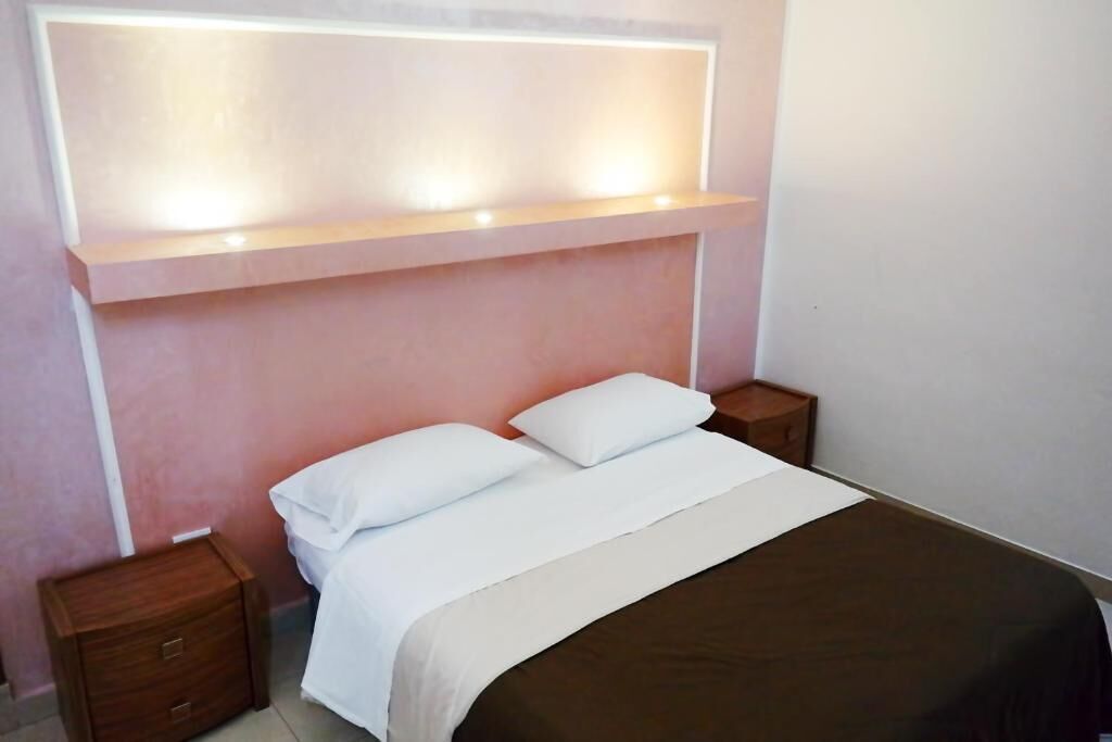 Een slaapkamer met een bed, twee nachtkastjes en een wandplank boven het bed.