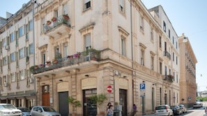 A corner building with multiple floors, large windows, and balconies with potted plants. - Fourseasons (Lecce)