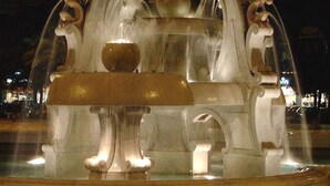 A fountain with multiple tiers and water jets, set in an urban environment at night. - Fourseasons (Lecce)
