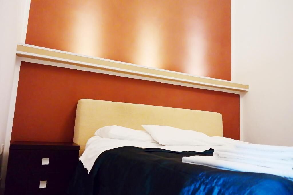 A bed with white and black bedding, a beige headboard, and a dark nightstand with drawers.