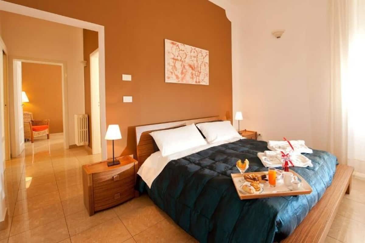 A neatly arranged bedroom with a bed, bedside tables, a tray of breakfast items, and a painting on the wall.