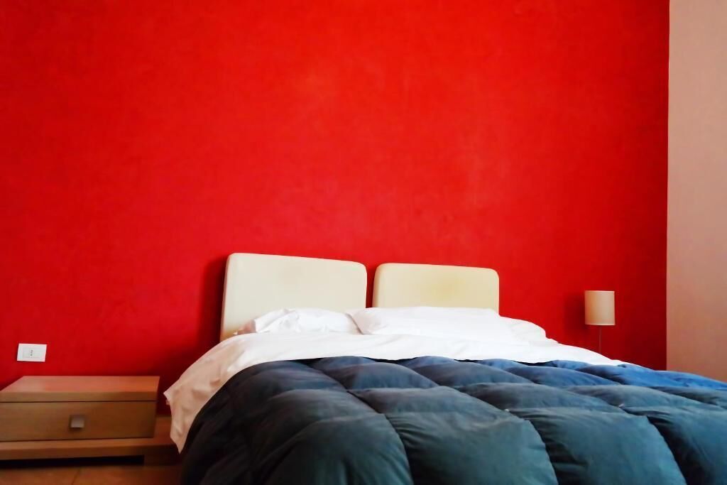 Un letto con una testiera bianca e una coperta blu e nera, davanti a una parete rossa.