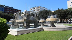 A public fountain with multiple water jets, surrounded by a well-maintained lawn and a few trees. - Fourseasons (Lecce)