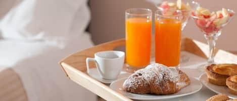 Bandeja de desayuno con pasteles, una taza de café y dos vasos de zumo de naranja sobre una mesa de madera.