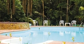 Ein Swimmingpool mit weißen Liegestühlen und einer Steinumrandung, umgeben von üppiger Vegetation.