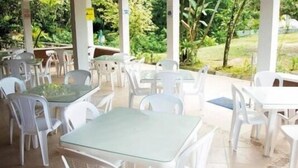 Een terras buiten met witte plastic tafels en stoelen, omgeven door groen.