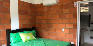 Ein Zimmer mit Backsteinwand, einem Bett mit blumigem, grünem Bettbezug, einem schwarzen Kopfteil und einer weißen Klimaanlage.