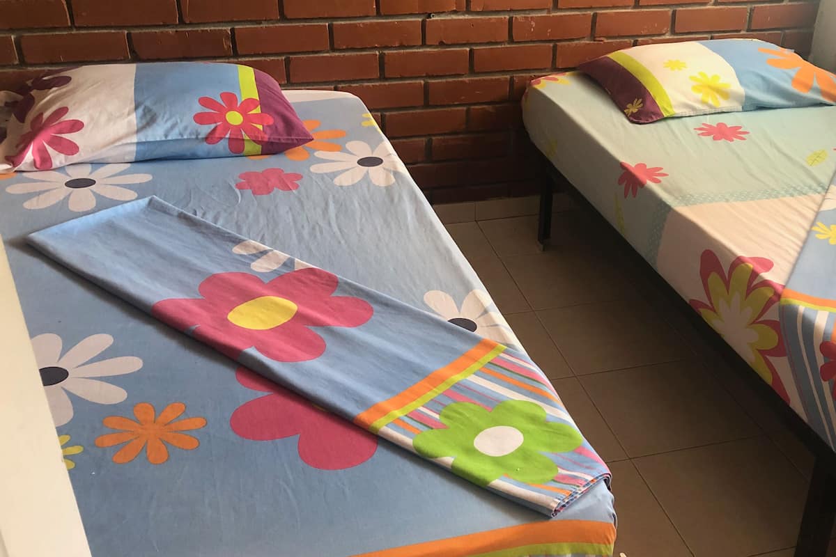 Deux lits simples avec une literie à motifs floraux, un mur en briques et un sol carrelé.