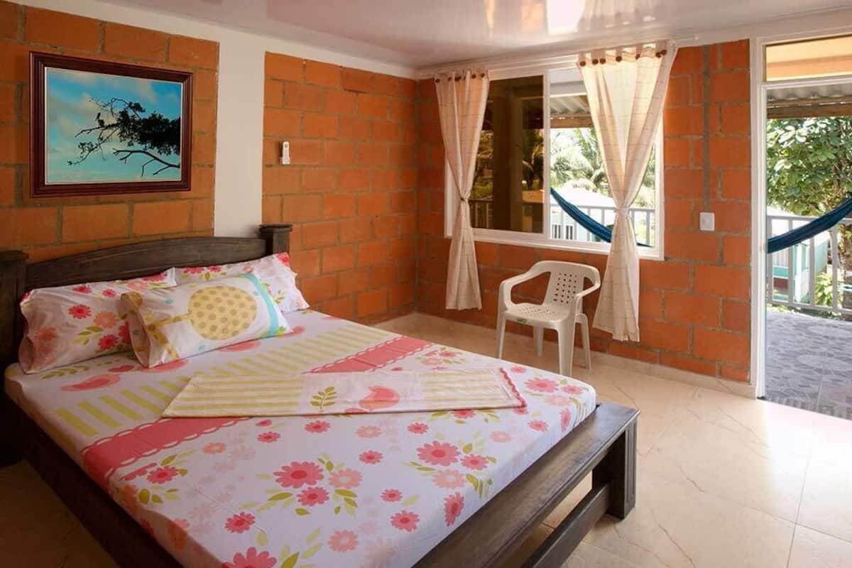 Une chambre à coucher avec un lit, une chaise, une fenêtre avec des rideaux et un tableau accroché au mur.