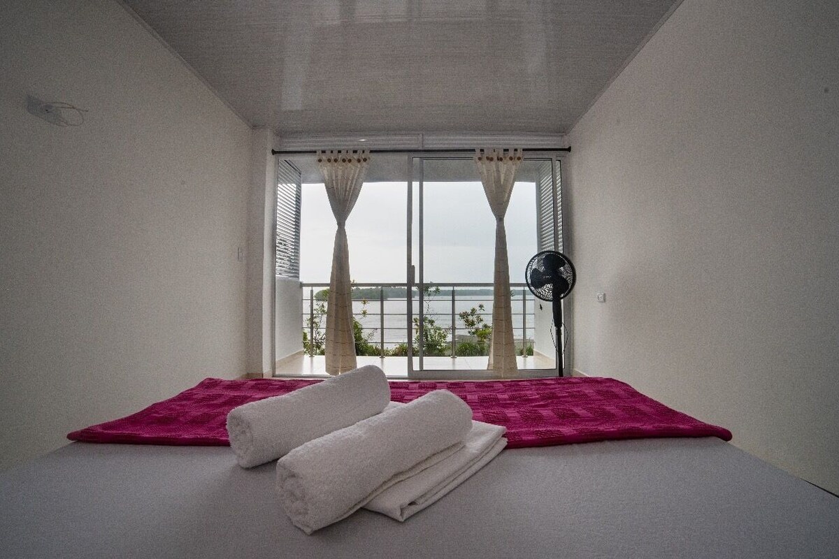 Une chambre avec un lit, une fenêtre avec des rideaux et un ventilateur.