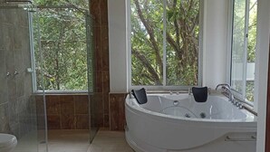 Un baño con cabina de ducha de vidrio, una bañera grande con vistas al exterior y un inodoro.