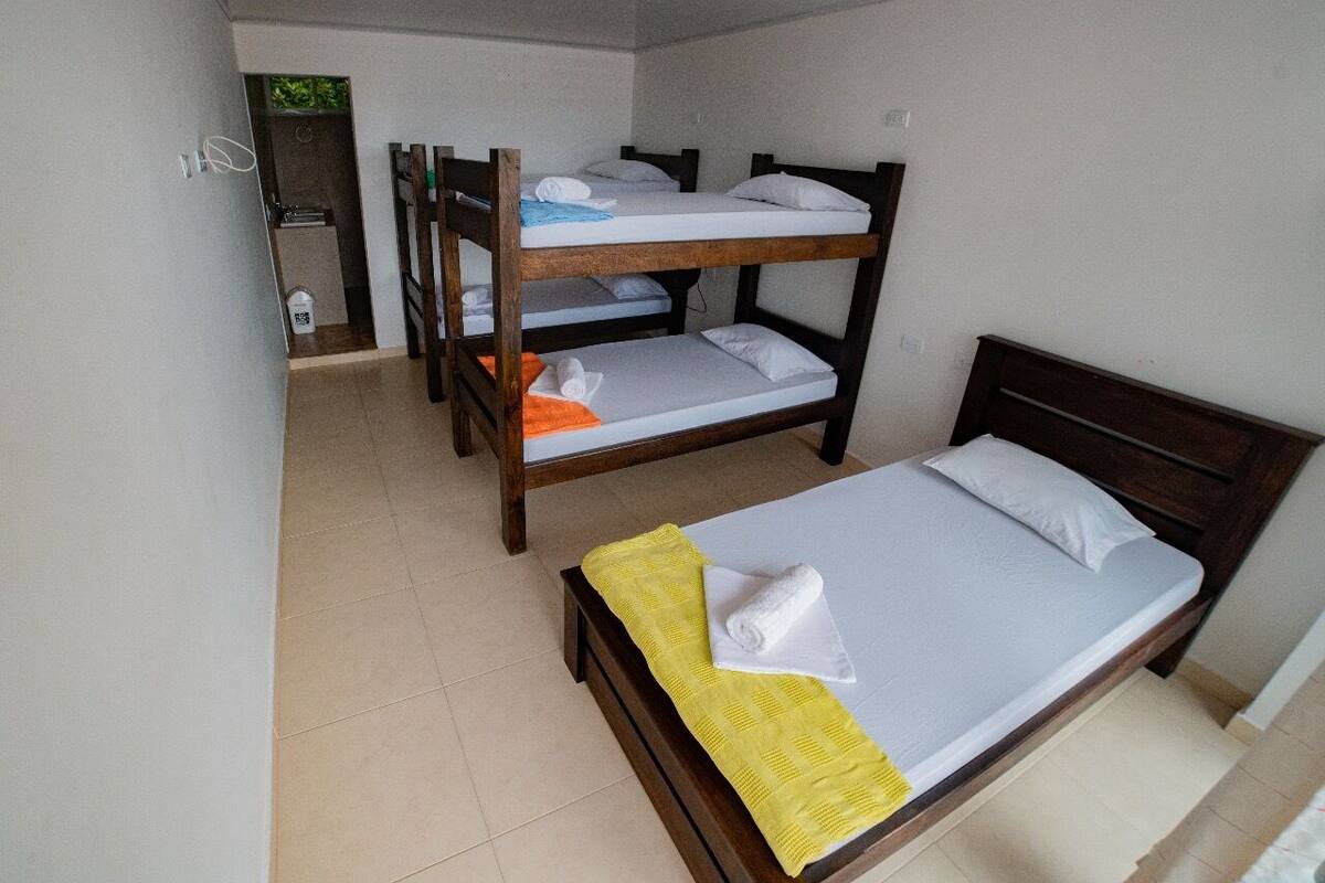 Una habitación con literas y una cama individual, un baño pequeño y un bote de basura.
