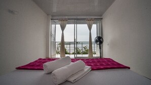 Una habitación con una cama, una ventana con cortinas y un ventilador.