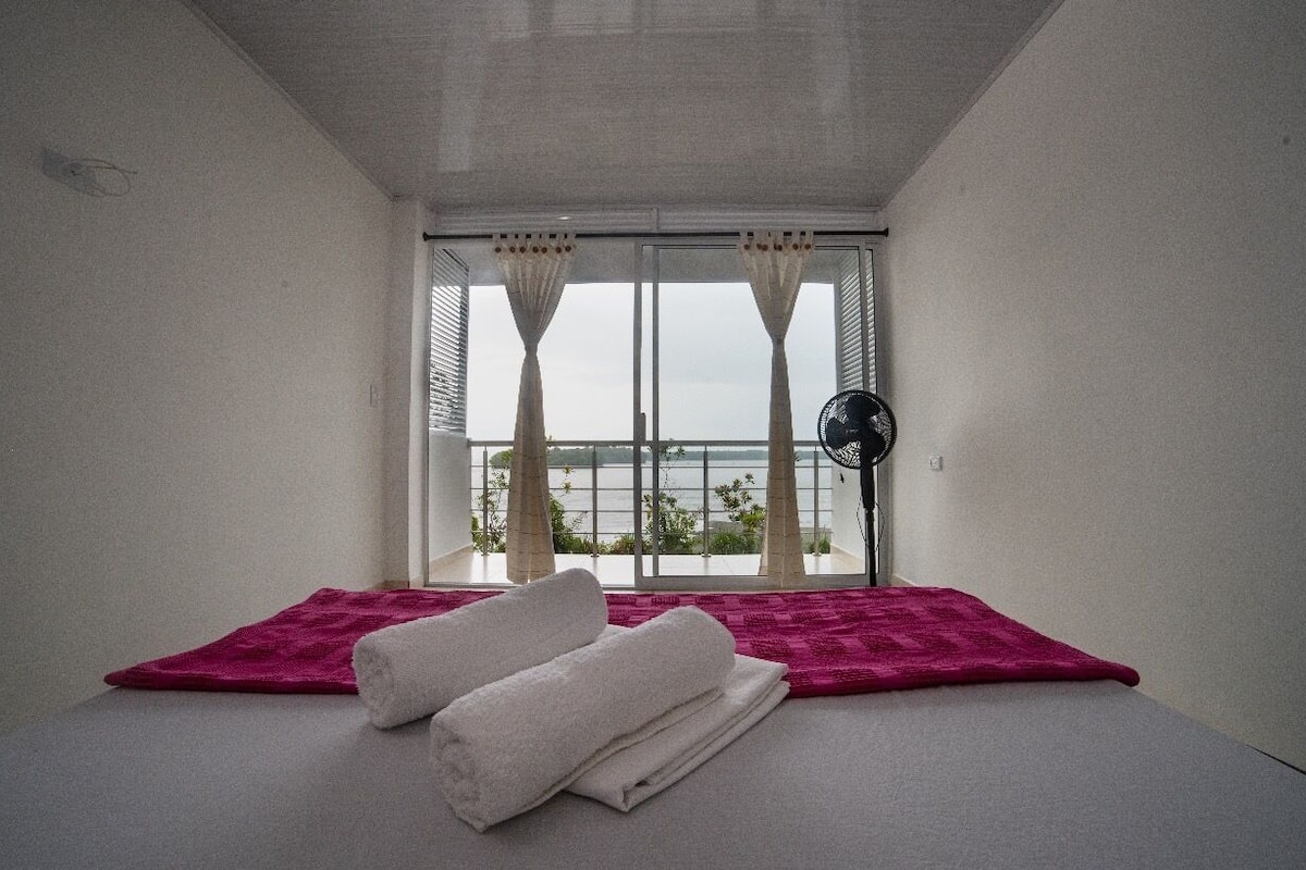 Una habitación con una cama, una ventana con cortinas y un ventilador.