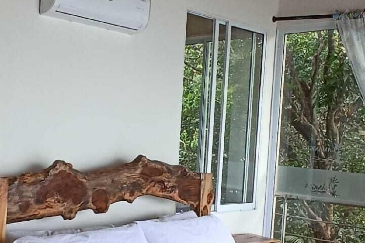 Un lit avec une tête de lit en bois, une literie blanche et une vue sur les arbres par la fenêtre.