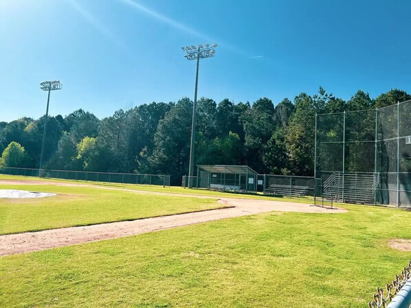 A baseball field with a dirt path, green grass, and a covered seating area.