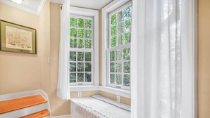 Una habitación en esquina con ventanal saliente, un cuadro en la pared y un banco de madera.