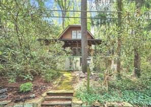 Escape to a secluded cabin surrounded by lush greenery and trees, with a front porch and stone staircase.