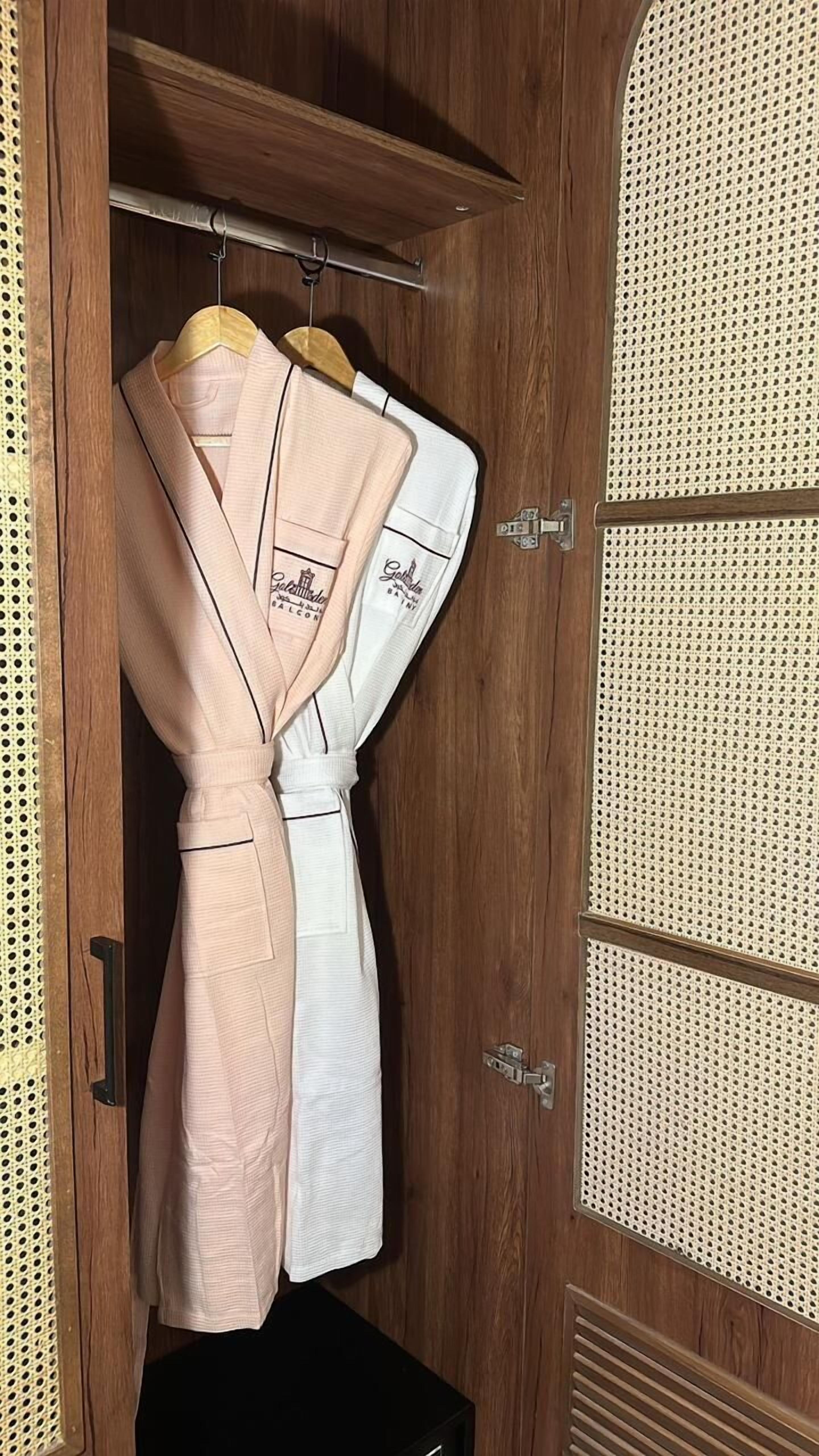 Un armario de madera con dos colgadores, uno rosa y otro blanco, con texto bordado.