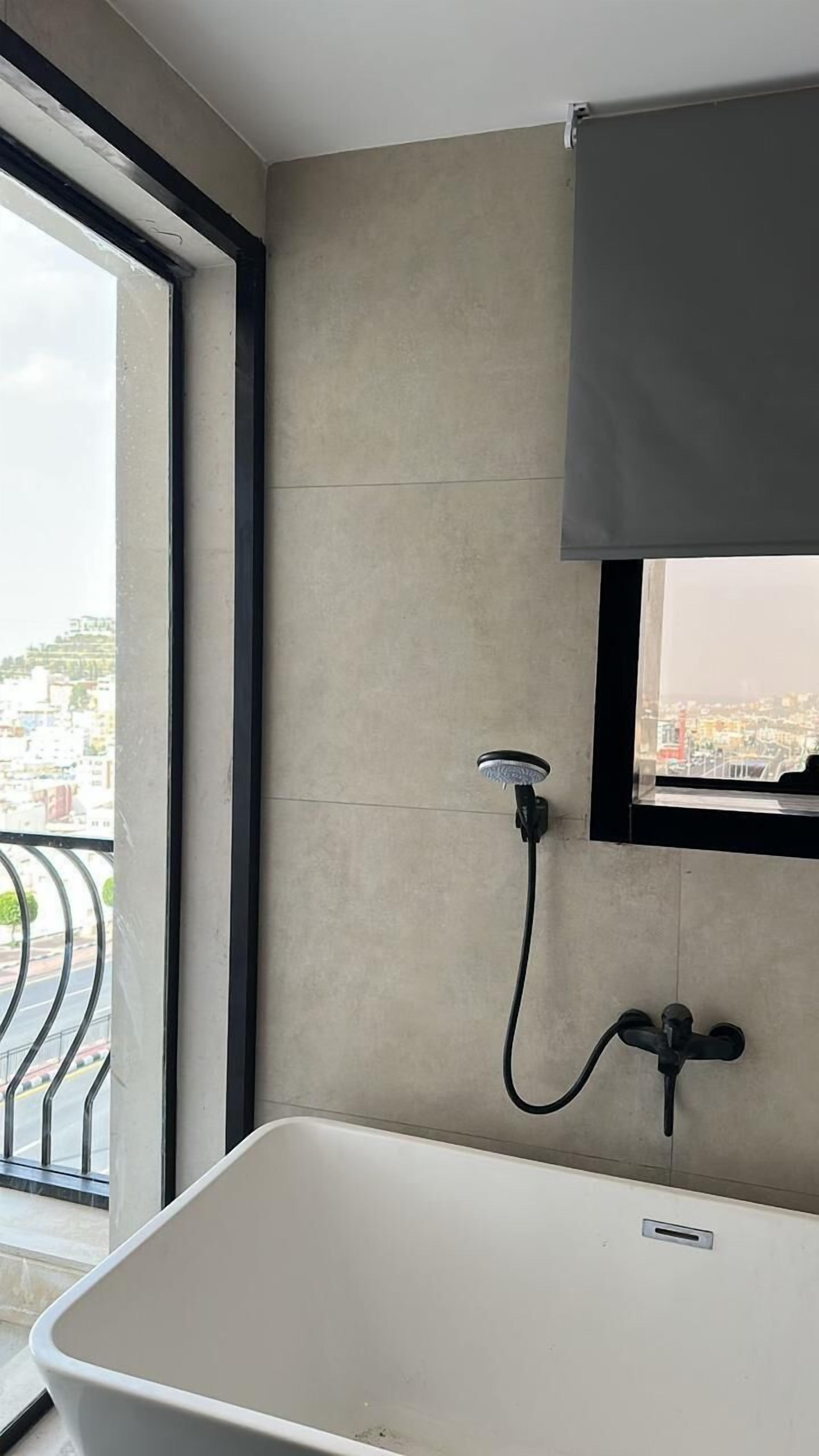 Un baño moderno con una bañera, un cabezal de ducha y un ventanal con vista a un paisaje urbano.