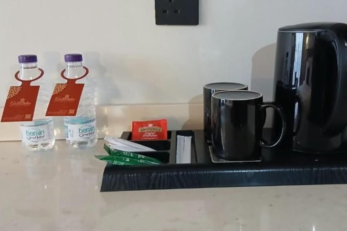 A hotel room with a coffee station featuring a coffee maker, two mugs, and bottled water.