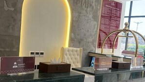 Un mostrador de recepción de hotel con diseño moderno, que incluye un letrero de neón, un sillón cómodo y una fuente decorativa.