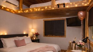 A bedroom with a bed, bedside table, lamp, and a window with a view.