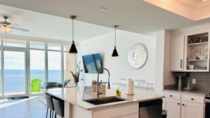 Una cucina moderna con una grande isola, zona pranzo con sedie, vista sull'oceano e un balcone.