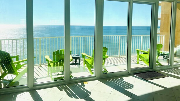 Un balcone con ampie finestre vista mare, sedie verdi e un tavolino.
