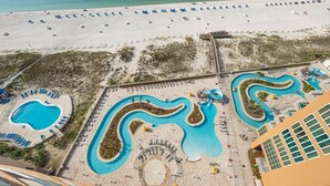 Vista aerea di un resort con un'ampia area piscina, spiaggia e un edificio dal design moderno.