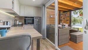A modern kitchen with a built-in oven and refrigerator, a dining area with a table and chairs, and a sliding glass door leading to an outdoor seating area with wicker furniture. - Beach House IVE –Romantic escape with jacuzzi, pool & olive grove charm in Pomer (Pomer)