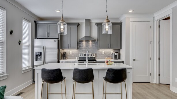 A modern kitchen with a central island, bar stools, and pendant lighting.