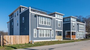 A modern multi-story residential building with a flat roof, large windows, and a wooden fence.