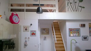 Una cocina con una escalera de madera, un reloj rojo y diversas decoraciones en la pared, incluyendo un póster y una fotografía enmarcada.