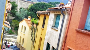 Una calle estrecha con edificios coloridos, una tienda a la vista y un muro de piedra al fondo.