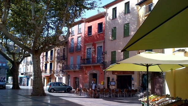 Una calle con mesas al aire libre, un coche estacionado en la acera y edificios con balcones.