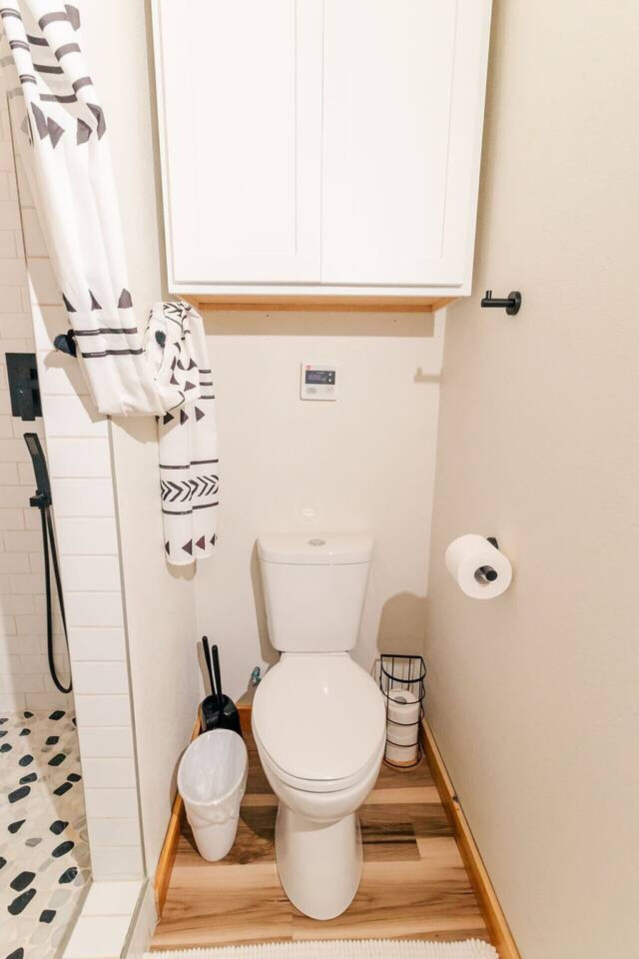 A compact bathroom with a toilet, a shower, and a towel rack.