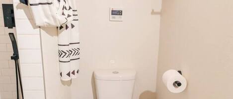 A compact bathroom with a toilet, a shower, and a towel rack.