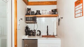 A compact kitchen with white cabinets, a stainless steel refrigerator, a coffee maker, and a microwave. - The Maple Casita at Selah Place (Athens)