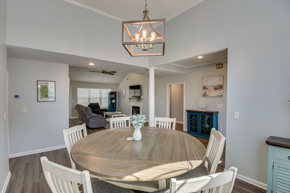 A dining area with a round wooden table, white chairs, and a hanging light fixture.