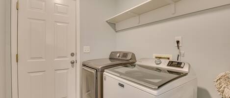A laundry room with a front-loading washer and dryer, a white door, and a shelf above the dryer.