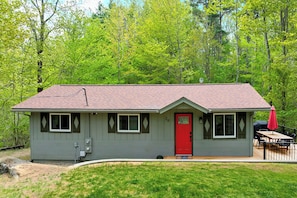 A small, single-story house with a red door, a deck, and a covered outdoor seating area. - Cozy, Pet-Friendly Escape Near Lake & Mountains (Gilford)