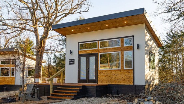 Una moderna cabina con facciata in legno, un portico anteriore e una scala che conduce all'ingresso.