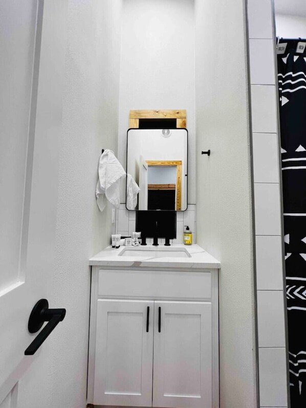 A bathroom with a white sink, mirror, and cabinets. There is a towel hanging on the wall and a bottle of hand soap on the counter.