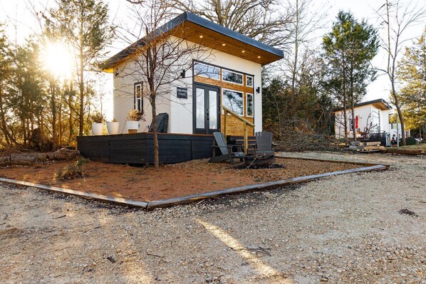 Una cabaña pequeña y moderna con terraza de madera y entrada de grava.