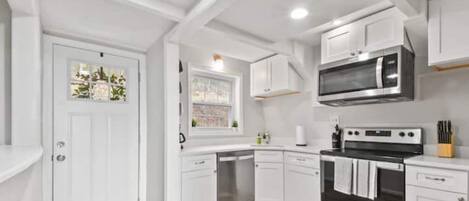 A modern kitchen with white cabinets, stainless steel appliances, and a wooden floor.