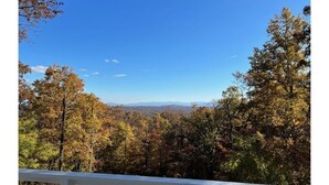 A view from a covered porch with a railing, overlooking a forested area with autumn foliage and distant mountains. - The Overlook (Winchester)